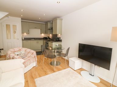 A kitchen and living room area with cabinets dining table chairs sofas and a television at The Moorings in Porthmadog