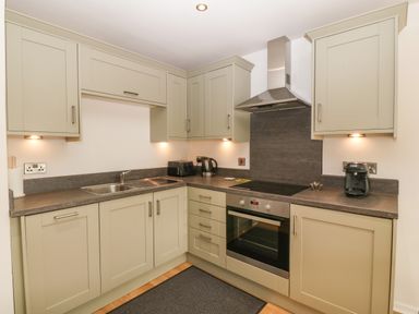 A kitchen with beige cabinets a stainless steel oven a stovetop a stainless steel sink and various small appliances on the counters at The Moorings in Porthmadog