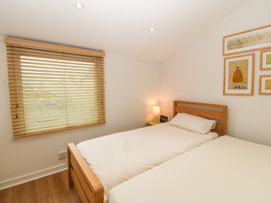 A bedroom with two single beds with wooden frames a window with wooden blinds and framed pictures on the wall at The Moorings in Porthmadog
