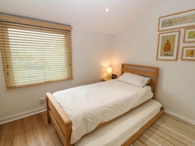 A bedroom with a wooden bed and a trundle bed underneath a window with wooden blinds at The Moorings in Porthmadog