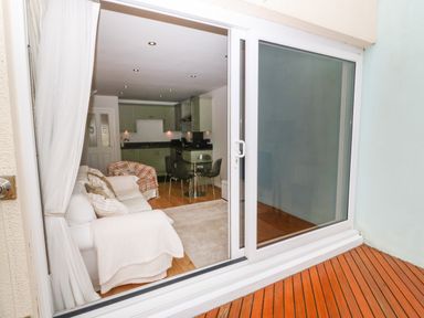 A view through sliding glass doors into a living room with white sofas and a kitchen area at The Moorings in Porthmadog