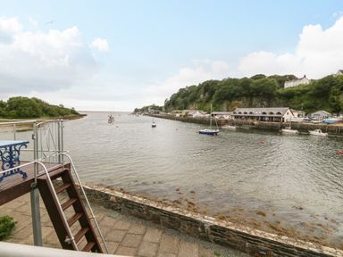 A river with boats moored near a stone wall and steps leading down at The Moorings in Porthmadog