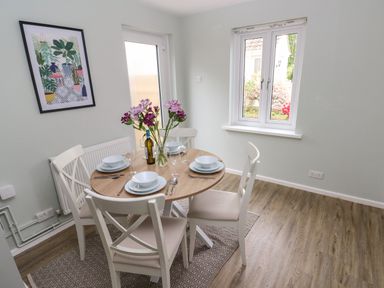 A dining area with a round wooden table set for four and white chairs near a window at Mews Cottage in Laugharne
