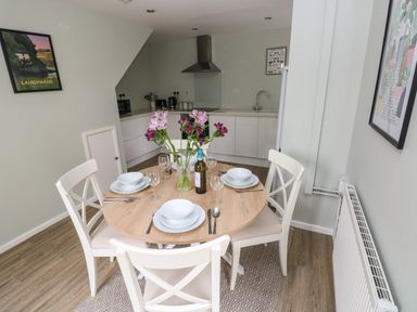 A kitchen and dining area with a round wooden table set for four and white chairs at Mews Cottage in Laugharne