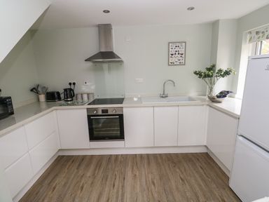 A kitchen with white cabinets wooden floor and appliances including oven toaster and refrigerator at Mews Cottage in Laugharne