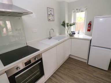 A kitchen with an oven and stovetop a sink a refrigerator a window and a fire extinguisher at Mews Cottage in Laugharne