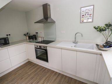 A kitchen with white cabinets oven stovetop microwave and sink at Mews Cottage in Laugharne