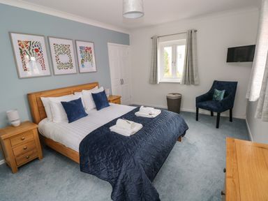A bedroom with a wooden bed and nightstands with lamps a window and a blue chair at Mews Cottage in Laugharne