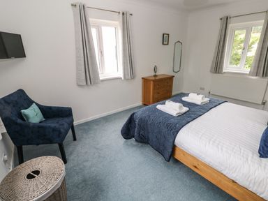 A bedroom with a bed with towels on it a blue armchair a wooden dresser and two windows at Mews Cottage in Laugharne