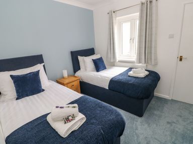 A bedroom with two single beds blue bedding a wooden nightstand with a lamp and a window at Mews Cottage in Laugharne