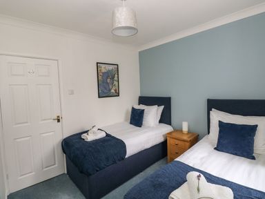 A bedroom with two single beds a wooden nightstand a door and a framed picture on the wall at Mews Cottage in Laugharne