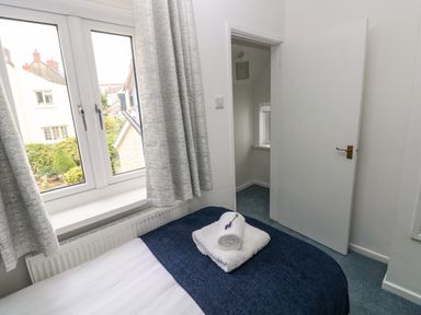 A bedroom with a bed covered by a blue blanket and white towels on top next to a window and an open door at Mews Cottage in Laugharne