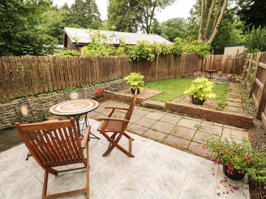 A garden with wooden chairs a small round table plants and a wooden fence at Mews Cottage in Laugharne