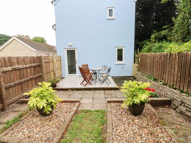 A backyard with a small patio set including a table and chairs beside a blue house at Mews Cottage in Laugharne