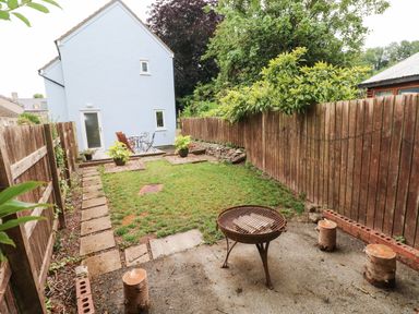 A backyard with a fire pit surrounded by wooden stools a small grassy area flower pots patio furniture and wooden fences at Mews Cottage in Laugharne