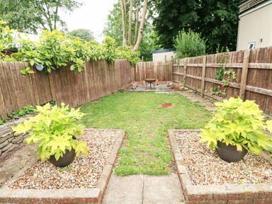 A fenced garden with grass and two plants in pots on gravel beds at Mews Cottage in Laugharne