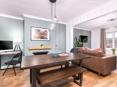 A dining area with a wooden table and bench next to a living room with a brown sofa and a wall-mounted TV at The View in Whitby