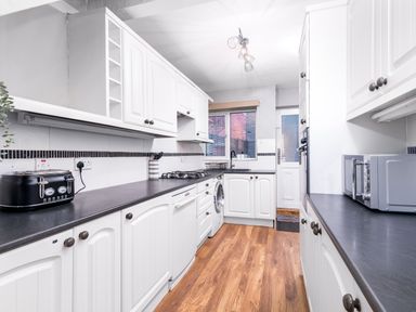 A kitchen with white cabinets black countertops and wooden floor at The View in Whitby