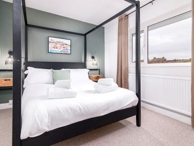 A bedroom with a black four poster bed two bedside tables wall lamps a window with brown curtains and a framed picture at The View in Whitby