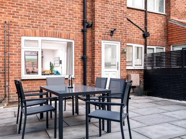 An outdoor patio with a glass table and six chairs in front of a brick house at The View in Whitby