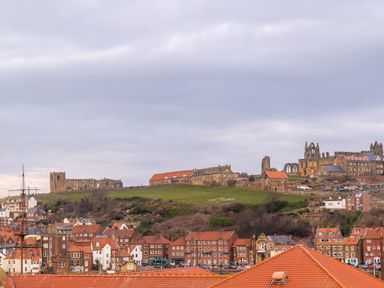 A town with red roof houses and old stone buildings on a hillside under a cloudy sky at The View in Whitby