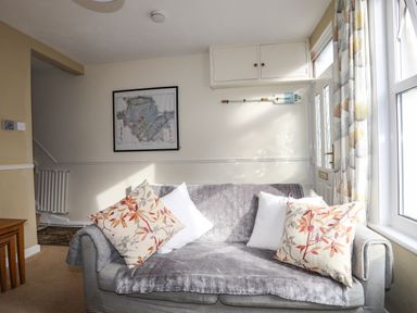 A living room with a gray sofa covered by a gray throw and four pillows with floral patterns and white cushions at Amelie Cottage in Beaumaris Anglesey