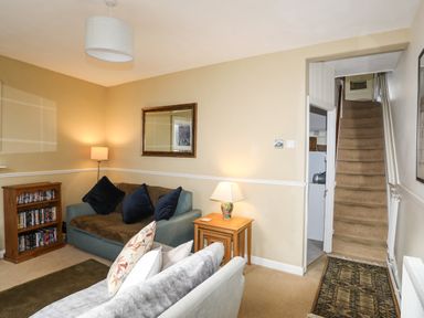 A living room with sofas a wooden bookshelf a side table with a lamp and carpeted stairs at Amelie Cottage Beaumaris Anglesey