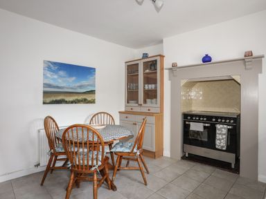 A dining area with a round table and four wooden chairs next to a cabinet and a stove at Amelie Cottage in Beaumaris Anglesey