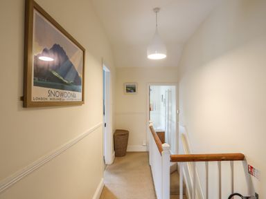 A hallway with a framed snowdonia poster a wicker laundry basket and a view into a bathroom at Amelie Cottage Beaumaris Anglesey