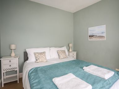 A bedroom with a double bed two bedside tables two lamps two pillows two folded towels and a painting on the wall at Amelie Cottage Beaumaris Anglesey