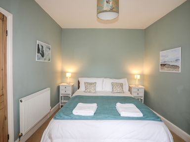 A bedroom with a bed in the center two bedside tables with lamps and paintings on the walls at Amelie Cottage Beaumaris Anglesey