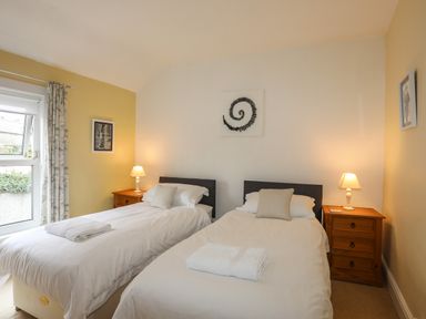 A bedroom with two single beds white bedding wooden nightstands and lamps at Amelie Cottage in Beaumaris Anglesey