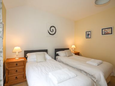 A bedroom with two single beds two bedside tables with lamps and artwork on the walls at Amelie Cottage in Beaumaris Anglesey
