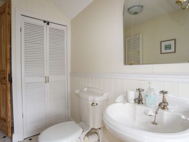 A bathroom with a toilet a sink a mirror and a closet with louvered doors at Amelie Cottage in Beaumaris Anglesey