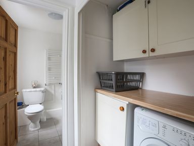 A laundry area with a washing machine and cabinets next to a bathroom with a toilet and towel radiator at Amelie Cottage Beaumaris Anglesey
