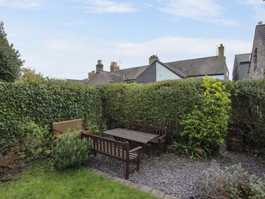 A garden area with wooden benches and a table surrounded by hedges and various plants at Amelie Cottage in Beaumaris Anglesey