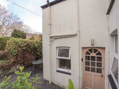 An outdoor area with a pink door and a small window on a white wall with metal table and chairs near a wall covered with ivy at Amelie Cottage in Beaumaris Anglesey