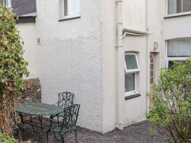 An outdoor seating area with a metal table and three chairs next to the corner of a white building with windows and a door at Amelie Cottage in Beaumaris Anglesey
