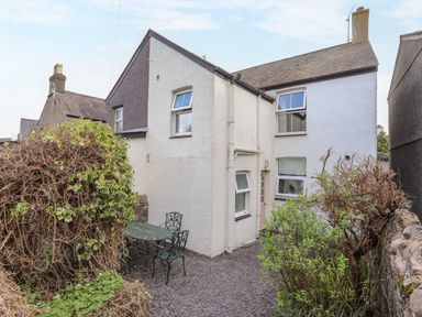 An outdoor space with a metal table and two chairs beside a white house with three visible windows and a door at Amelie Cottage in Beaumaris Anglesey