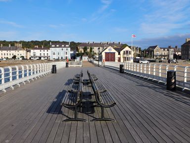 A pier with benches and railings leading to buildings on the shore at Amelie Cottage in Beaumaris Anglesey