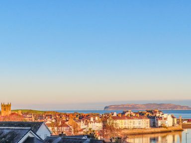 A coastal town with rooftops a church sea and an island in the background at Amelie Cottage in Beaumaris Anglesey