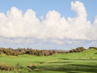 A golf course with a red flag and a small stream under a blue sky with clouds at Amelie Cottage in Beaumaris Anglesey