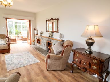 A living room with armchairs a fireplace a wooden chest with a lamp and a floral rug at Glebe Farm Cottage in Rathfriland County Down