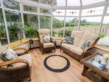 A sunroom with wicker armchairs and sofa around a round rug with windows showing a field at Glebe Farm Cottage in Rathfriland County Down