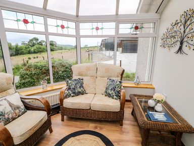 A sitting area with wicker furniture and cushions in a sunroom with stained glass windows at Glebe Farm Cottage in Rathfriland County Down