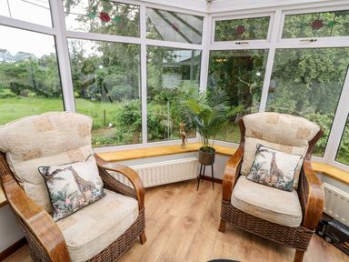 A conservatory with two wicker armchairs with cushions and a plant on a stand at Glebe Farm Cottage in Rathfriland County Down