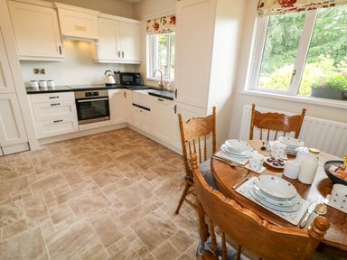 A kitchen with wooden dining table and chairs set with dishes next to white cabinets and black countertops at Glebe Farm Cottage in Rathfriland County Down
