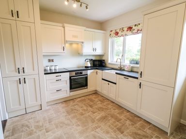 A kitchen with white cabinets black countertops an oven a sink under a window with floral blinds at Glebe Farm Cottage Rathfriland County Down