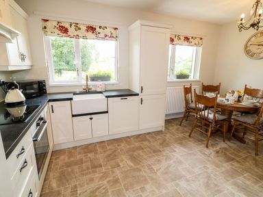 A kitchen with white cabinets a black countertop a white sink and a wooden dining table with chairs at Glebe Farm Cottage in Rathfriland County Down
