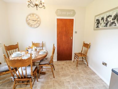A dining area with a wooden table set with dishes and mugs wooden chairs a wall clock a wooden door with a sign above it and a framed cow painting at Glebe Farm Cottage in Rathfriland County Down